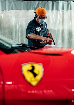 Auto body shop Los Angeles: Technician working on a red Ferrari, polishing the hood, Ferrari logo visible, repair shop setting.
