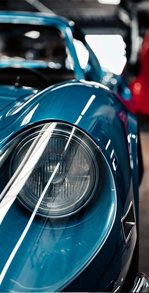 Luxury auto body shop Los Angeles: Close-up of a classic blue car headlight, detailing and reflections visible, high-end vehicle.