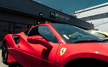 Luxury auto body shop Los Angeles: Red Ferrari 488 parked outside, shop sign visible, high-end vehicle repair facility.