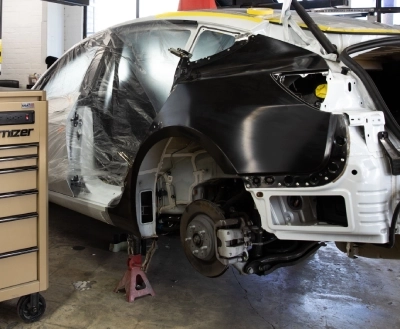Auto body collision repair: Damaged car wheel well, showing exposed suspension and brake rotor, repair in progress.