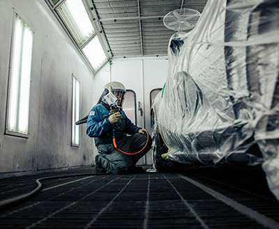 Preparing paintwork: Technician in safety suit blends colors, machinery and supplies in a professional paint mixing area.