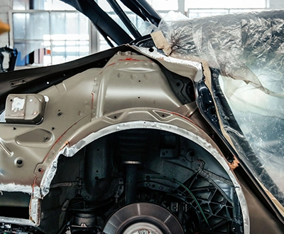 Structural repair: Car frame exposed, plastic covering protecting interior, door ajar in a garage setting, repair process visible.